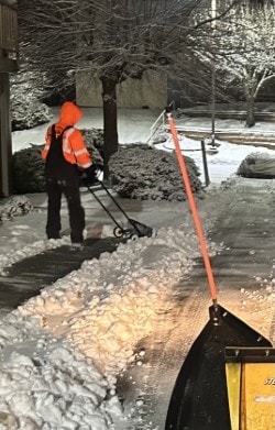 Snow blower clearing walkway at night
